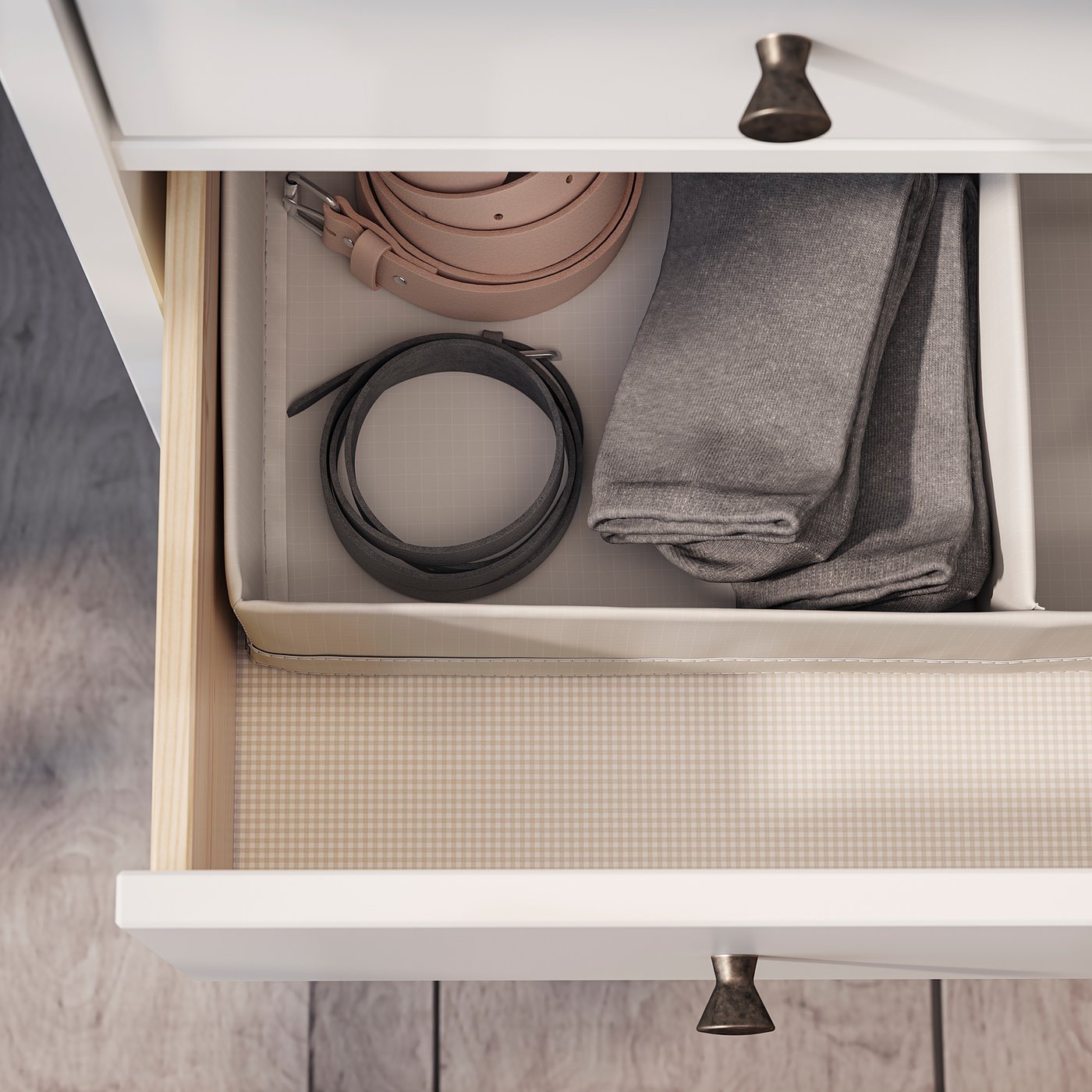 Open drawer with organised belts and folded grey clothes.