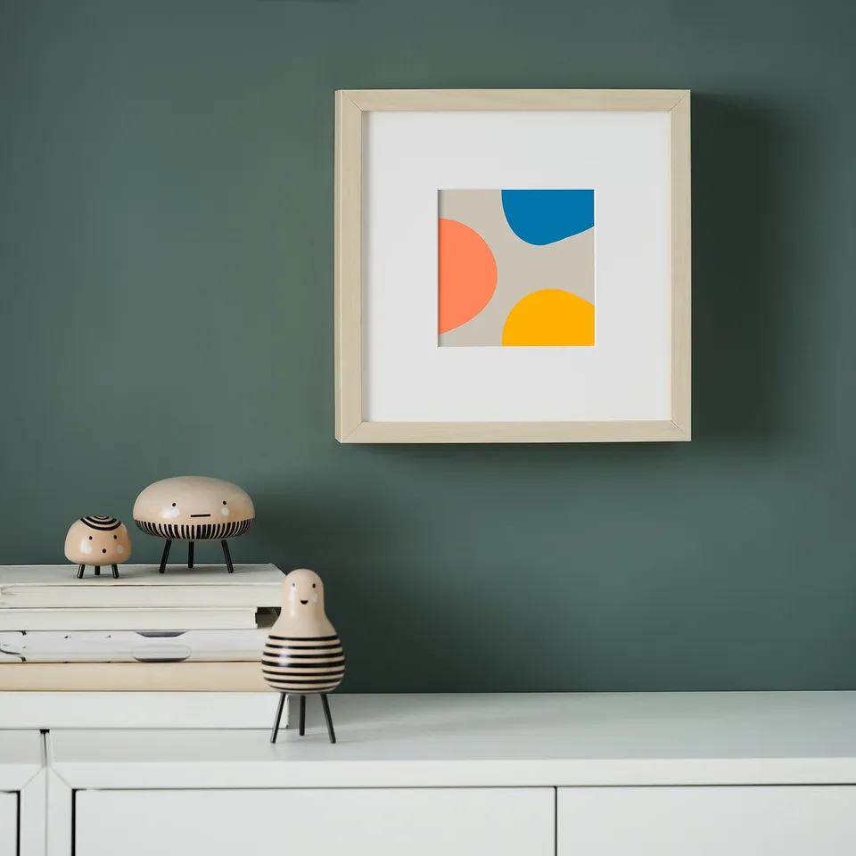 A teal wall displays a framed image with colourful shapes. Below, a table holds stacked papers and ceramic figurines.