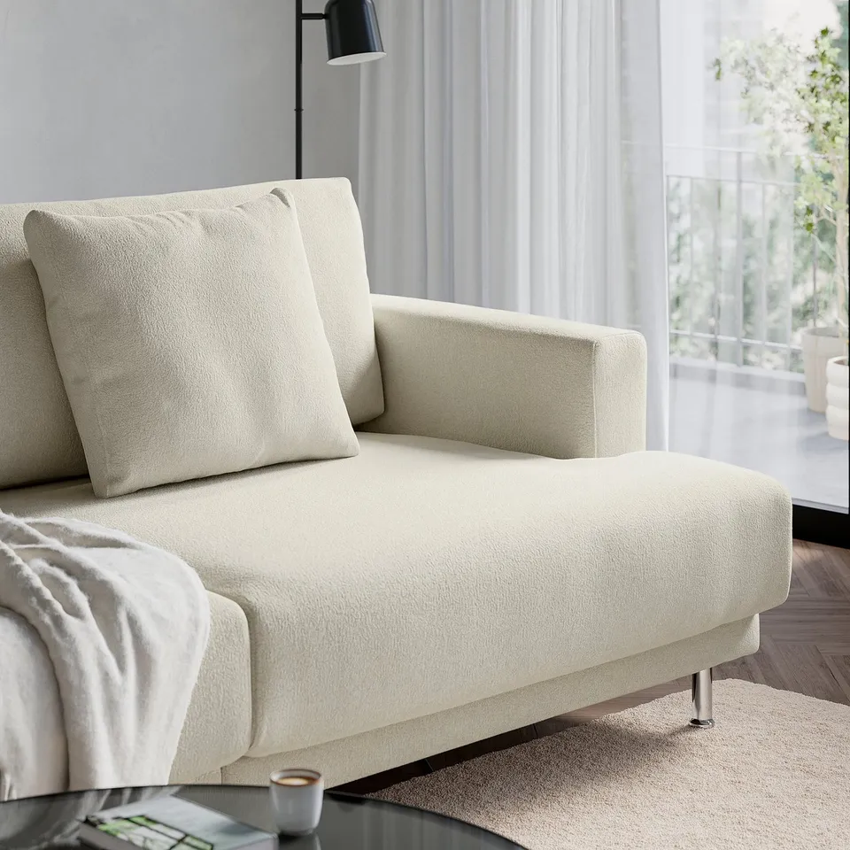 A modern, light-colored sofa with deep cushions sits near a window. The design is airy and comfortable, with a stylish, inviting appearance.