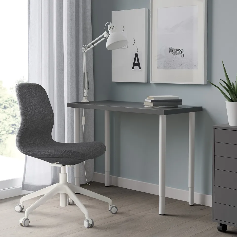 Black LINNMON desk with adjustable white legs, grey chair, lamp, books, & wall art.