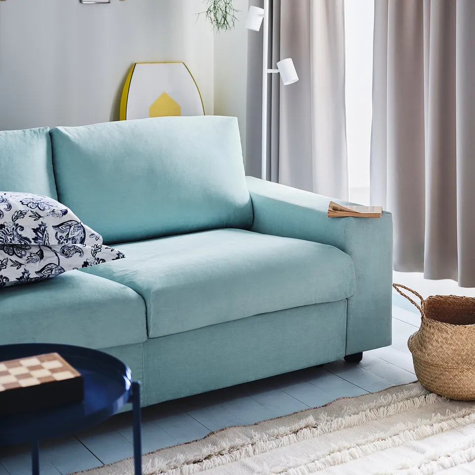 Bright living room with blue NYMÅNE floor lamp, light blue couch, decorative pillows, hanging plant, shelves, and grey curtains.