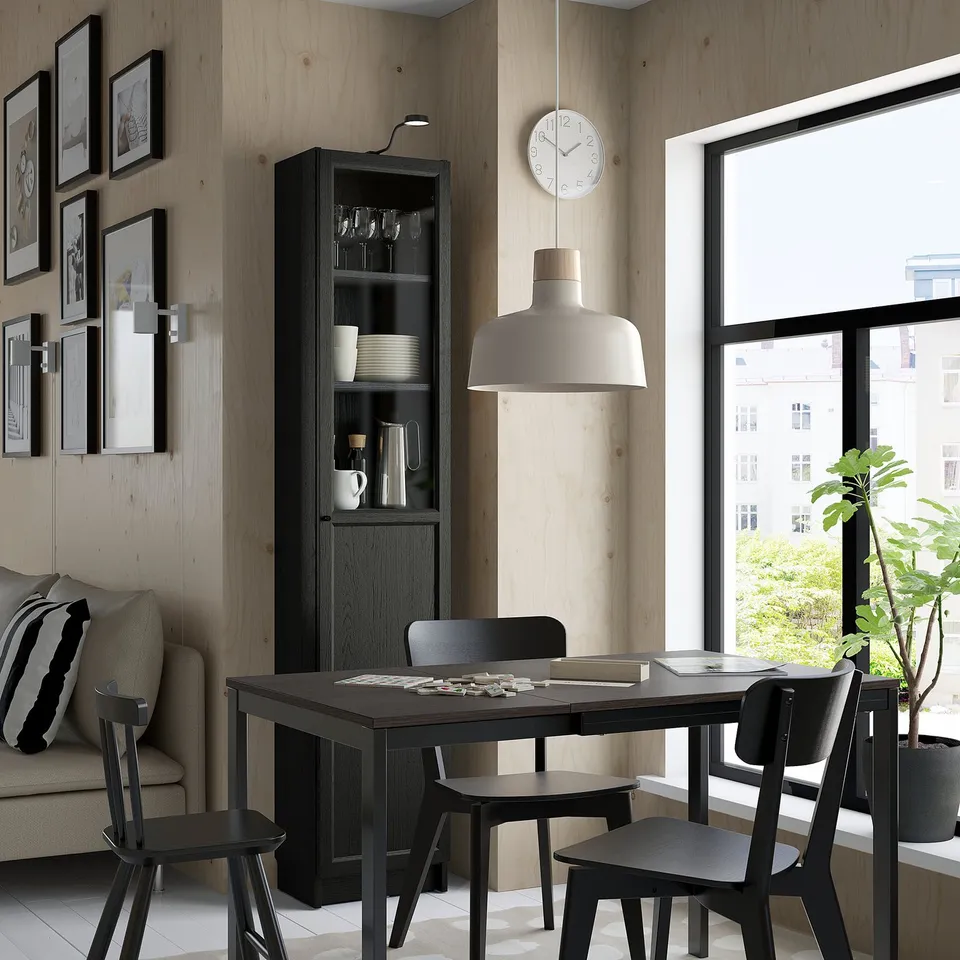 Modern dining area with black BILLY bookcase, light wood walls, large window, black table, chairs, and hanging lamp.