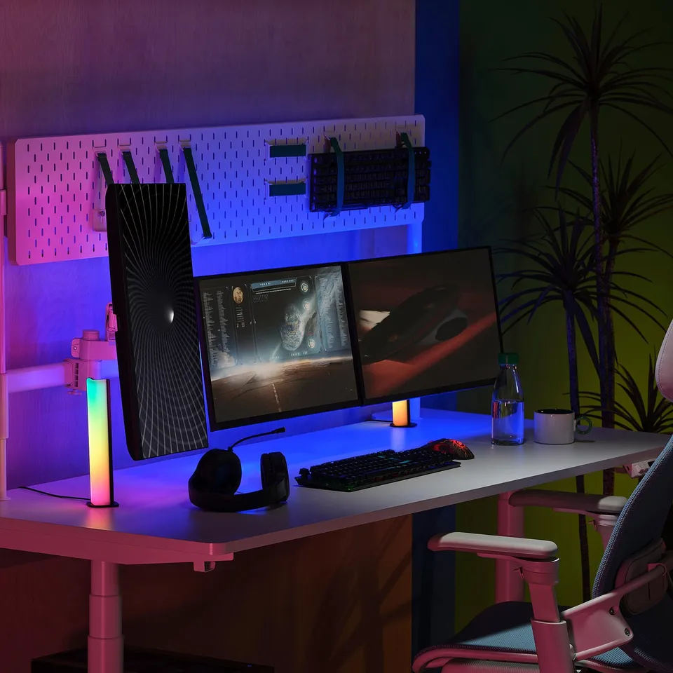 Pink home office with SKAFTSÄRV pegboard, dual monitors, green wall, palm plant.