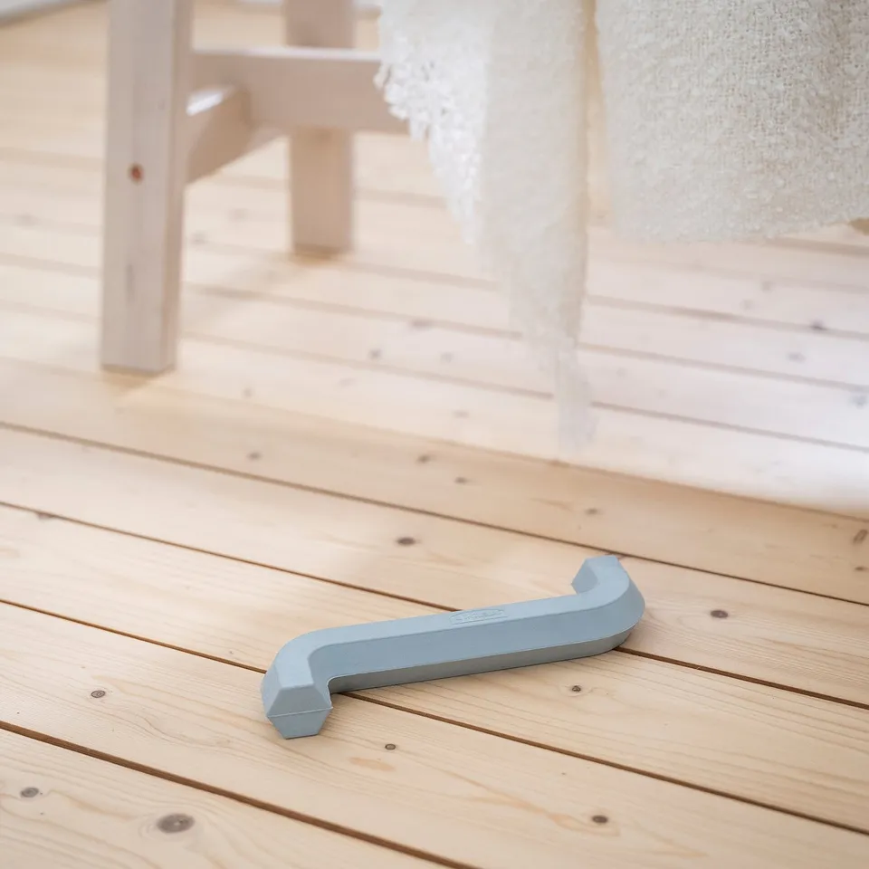 Blue dog toy on wooden floor, resembles an allen key with a playful, ergonomic design. Small but distinctive, laying next to a wooden table leg.