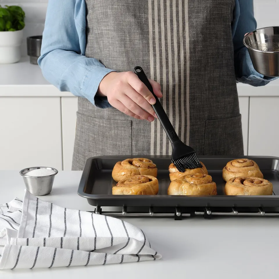 Person glazing baked goods with GRILLTIDER brush. Easy to store, spreads liquid evenly.