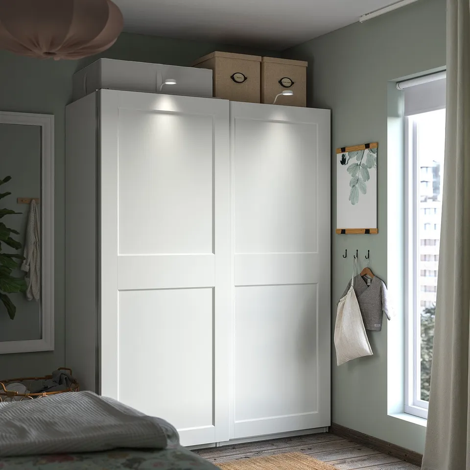 Modern white wardrobe with lights, storage, teal wall, near window.