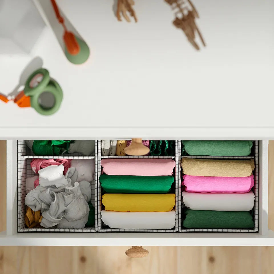 Open drawer with three dividers, neatly folded colourful clothes. Adjustable feet.