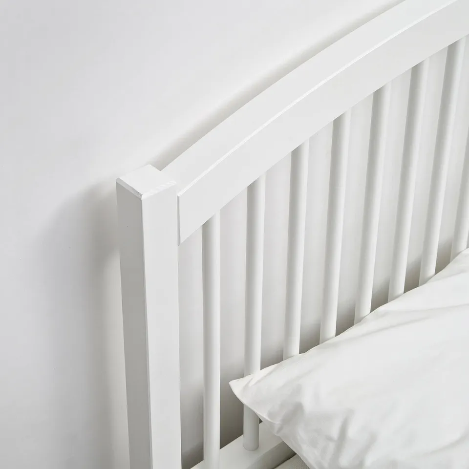 A clean, well-crafted white wooden bed, with sturdy spindles and a high headboard, ensuring comfort and durability.