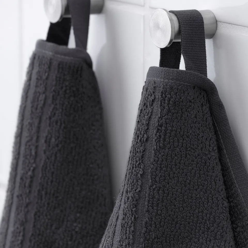 Two black VÅGSJÖN towels hang on hooks. One is folded; both are soft, absorbent, and quick-drying.