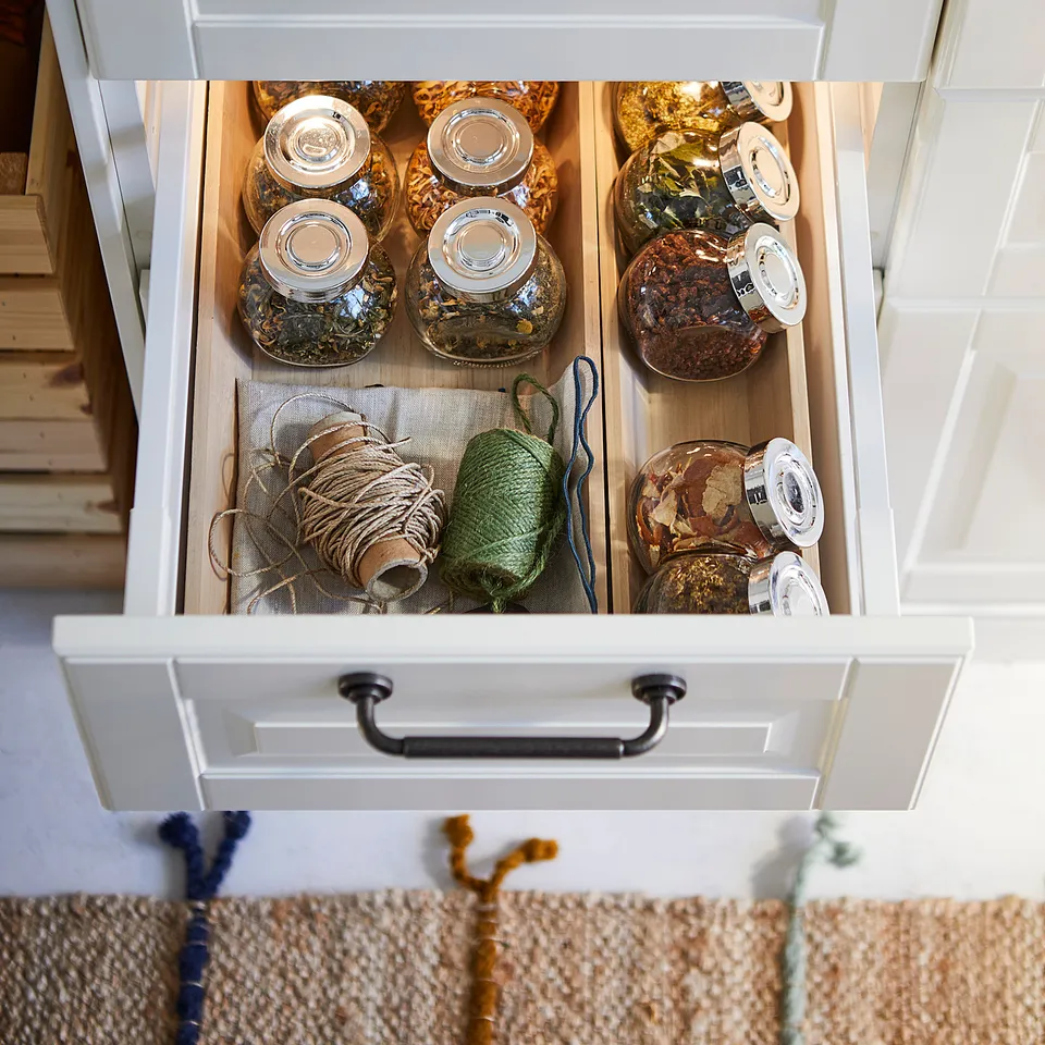 Drawer with multiple glass jars storing dried herbs and strings. Jars clear with metal lid, organised neatly. Wooden drawer, black handles.