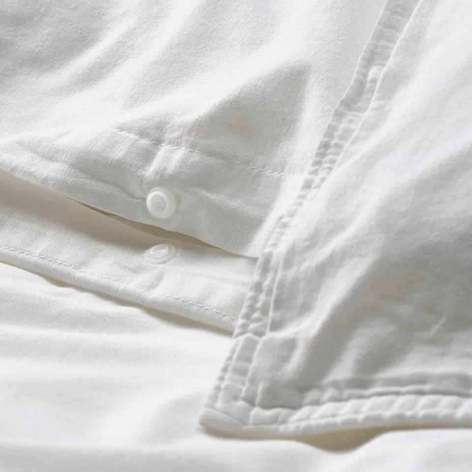 Close-up of white bed fitted sheet with elastic straps and poppers to secure mattress.
