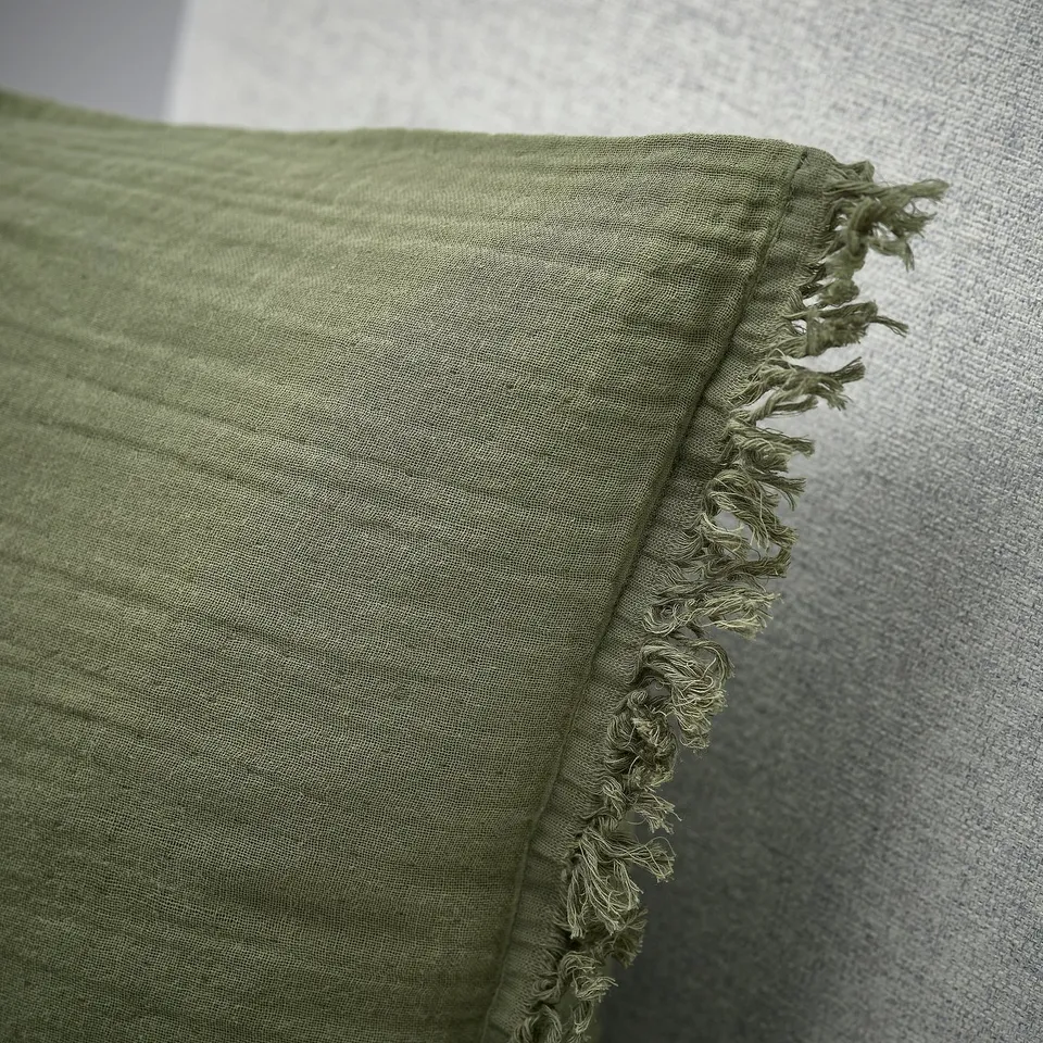 Folded light green cushion cover with fringed edges, showcasing soft, textured cotton material and neat stitching.