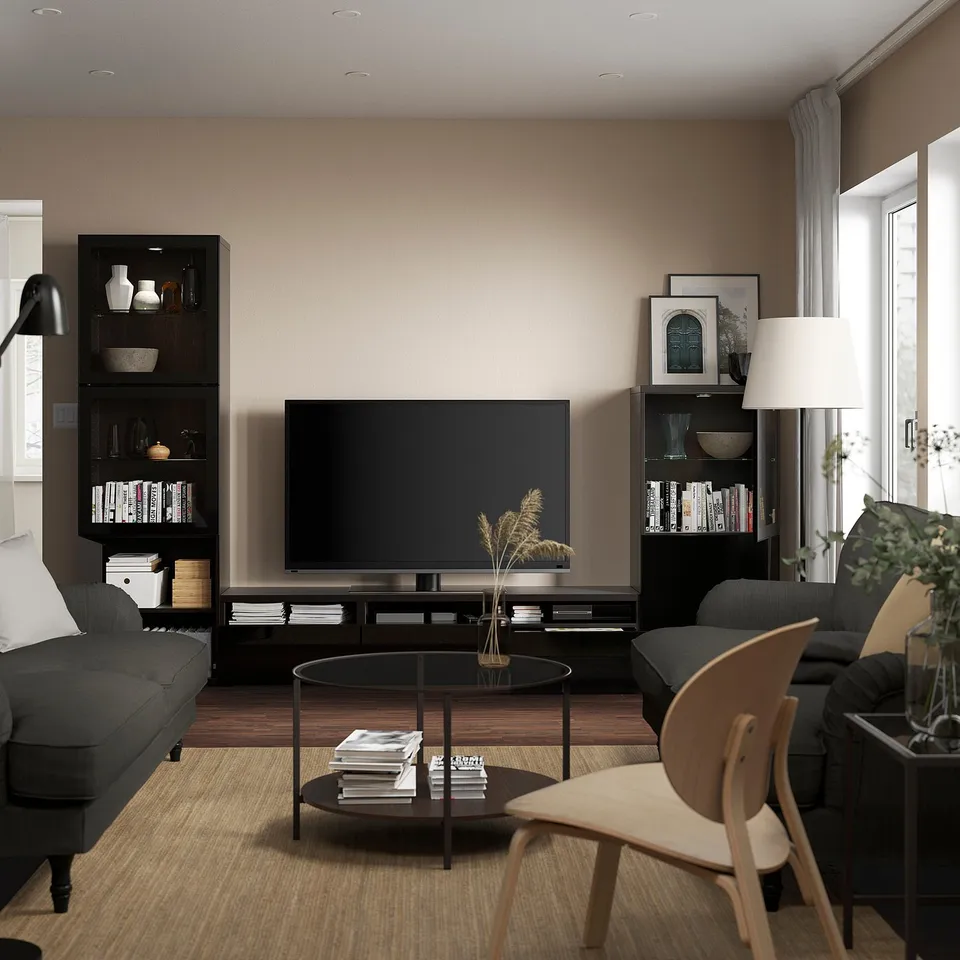 Modern living room with BESTÅ tv storage, flat-screen tv, two black sofas, round coffee table, wooden chair, large window.