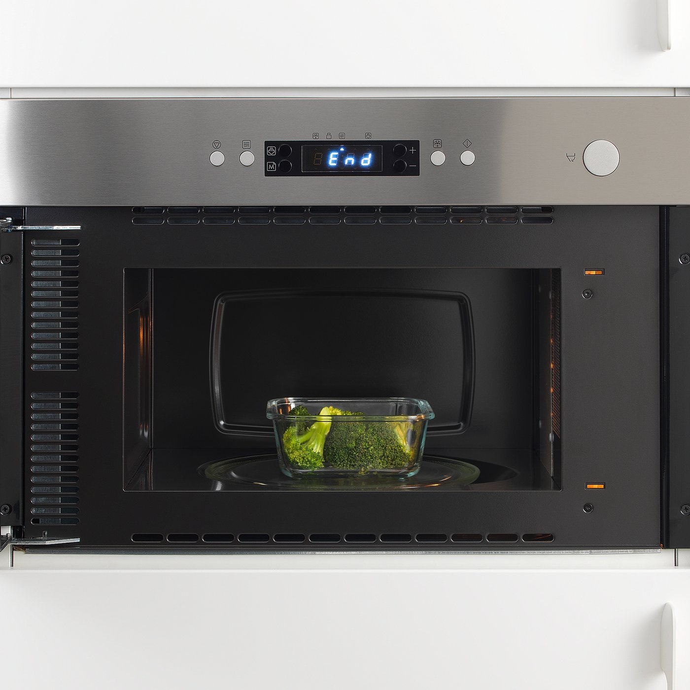 Built-in stainless steel microwave by IKEA 365+, displaying a digital clock and heating a glass container with broccoli.