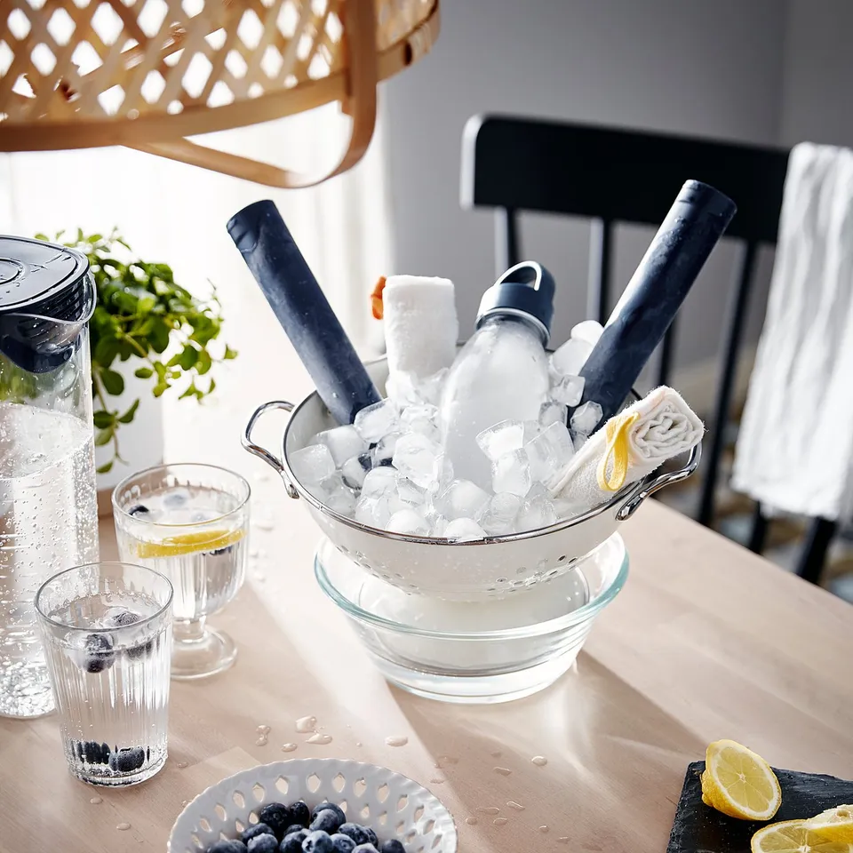 A refreshing drink setup with glasses, ice, lemon, blueberries, and water bottle on a dining table.