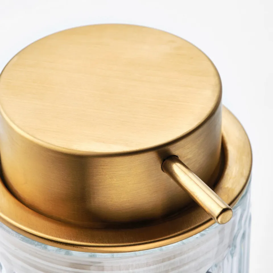 Golden metal soap dispenser top with handle over clear glass jar.
