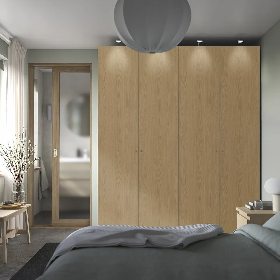 Bedroom with PAX wardrobe & lighting, adjacent bathroom with mirror door. Bed with grey bedding and bedside table with lamp.