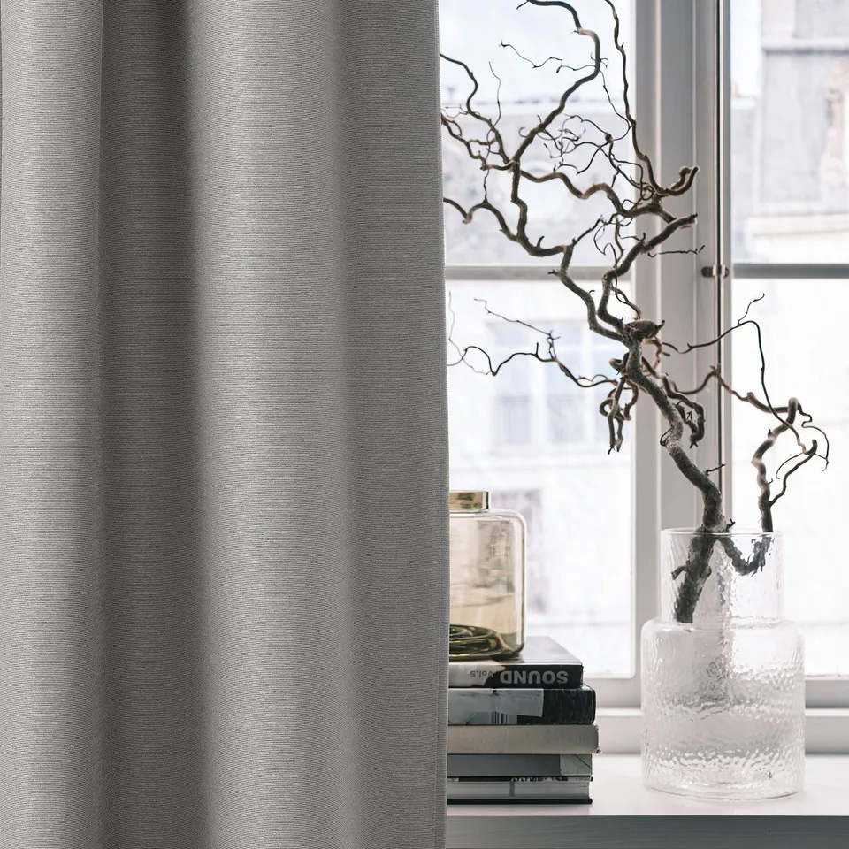 VILBORG grey room darkening curtain with linear texture near window, books, and a clear vase with branches.