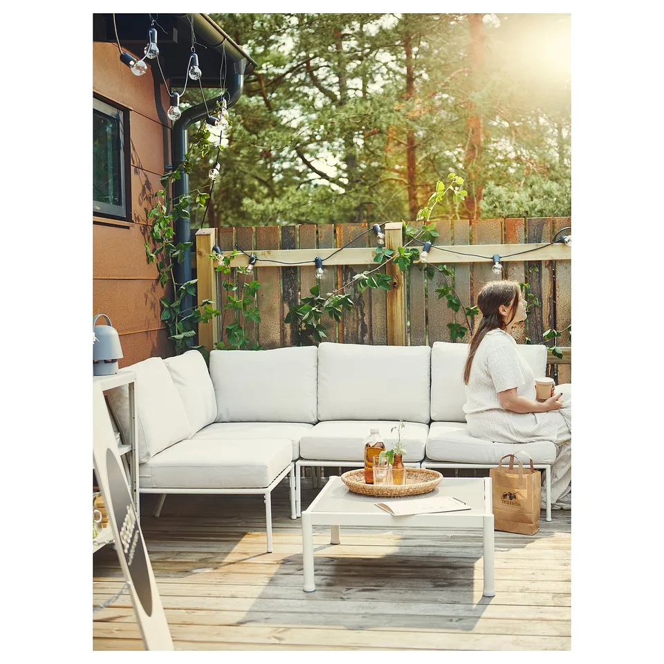 Person relaxing on l-shaped sectional sofa on wooden deck, with lights and fence.