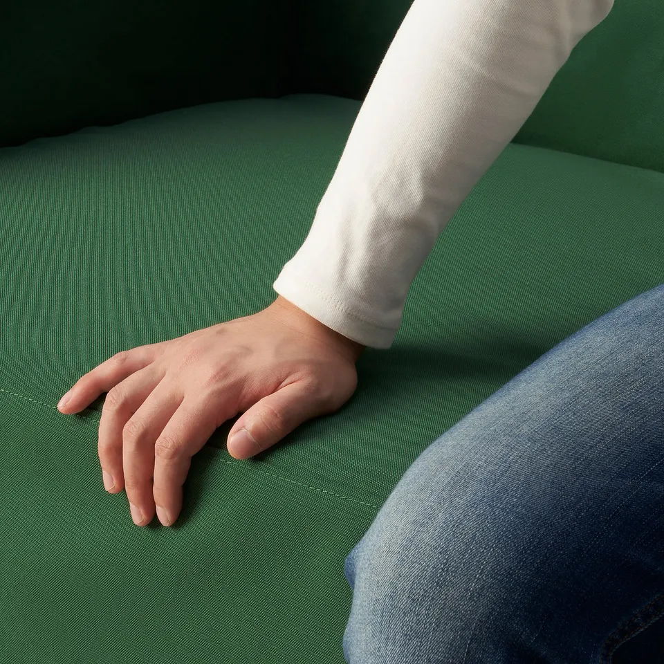 Person resting arm on green cushioned surface; white sleeve, jeans visible.