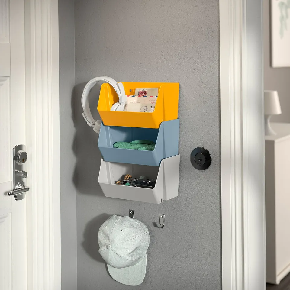 Wall-mounted organiser with yellow, blue, and white bins and a hanging white hat.