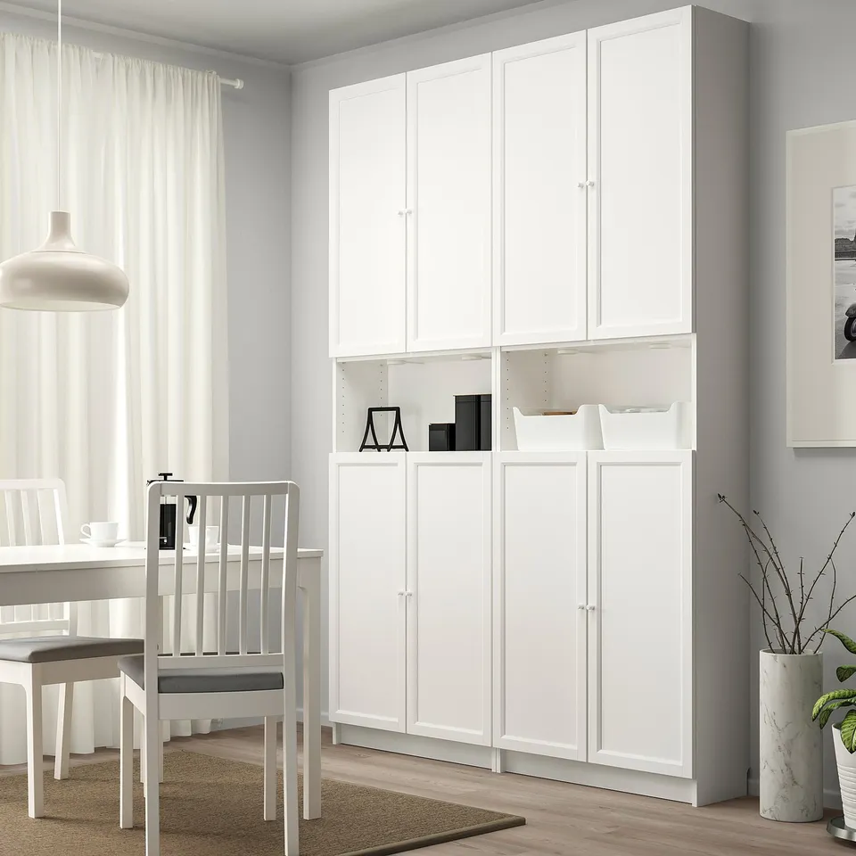 White BILLY bookcase with panel doors, tall, between table and window, ample storage.
