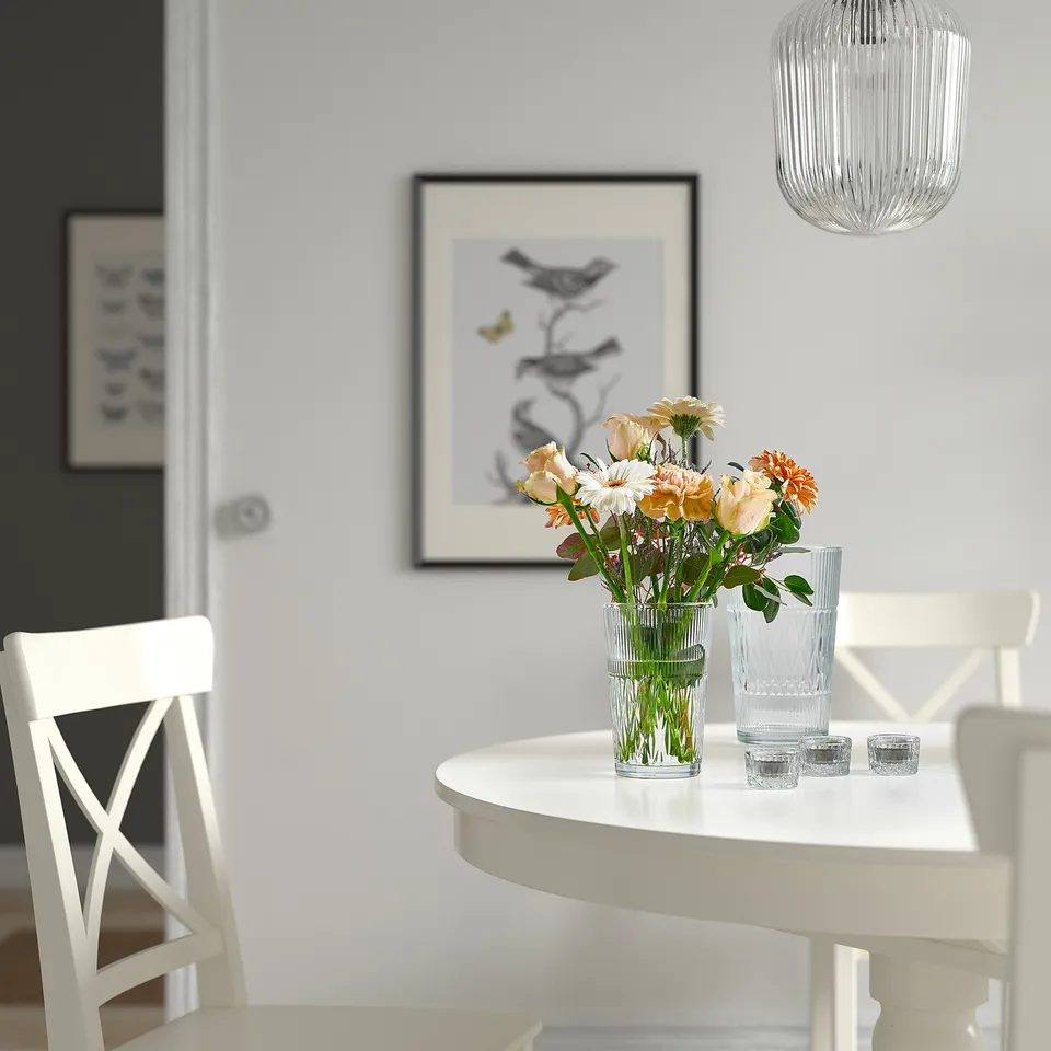 Small glass vase with flowers on a white table, next to tall glass.