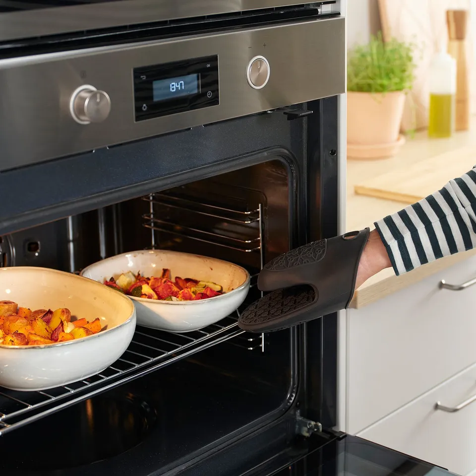 Person using oven mitt to remove dishes from oven. The mitt protects hands and provides a firm grip.