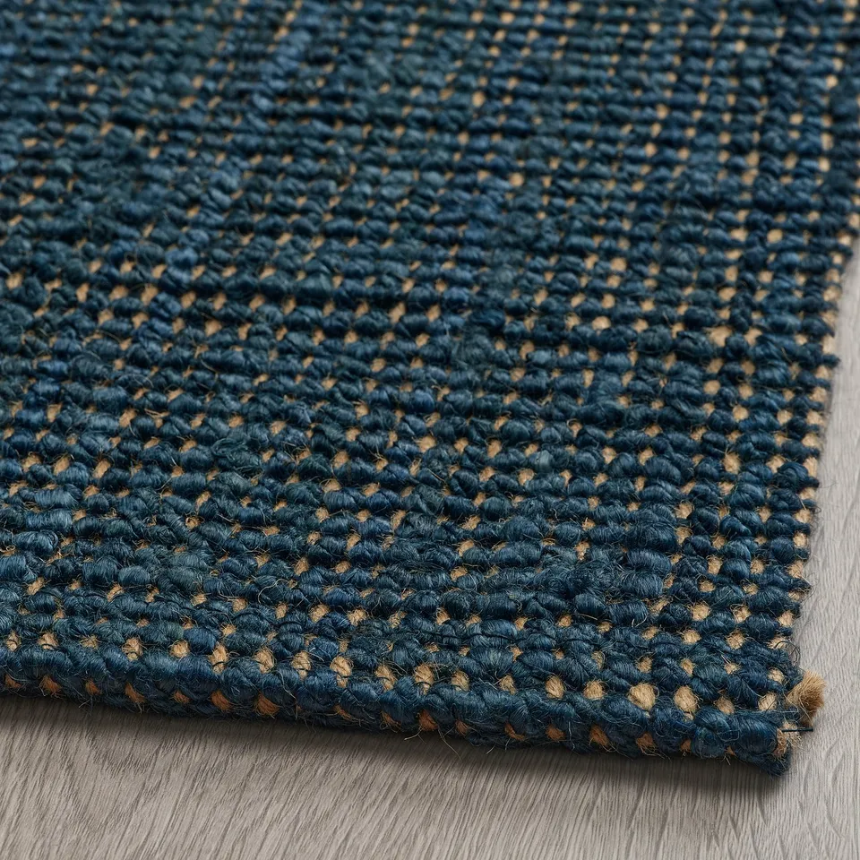 Dark blue woven jute rug with intricate texture, laid on wooden floor, showcasing its natural, rustic weave and warm, cosy appeal.