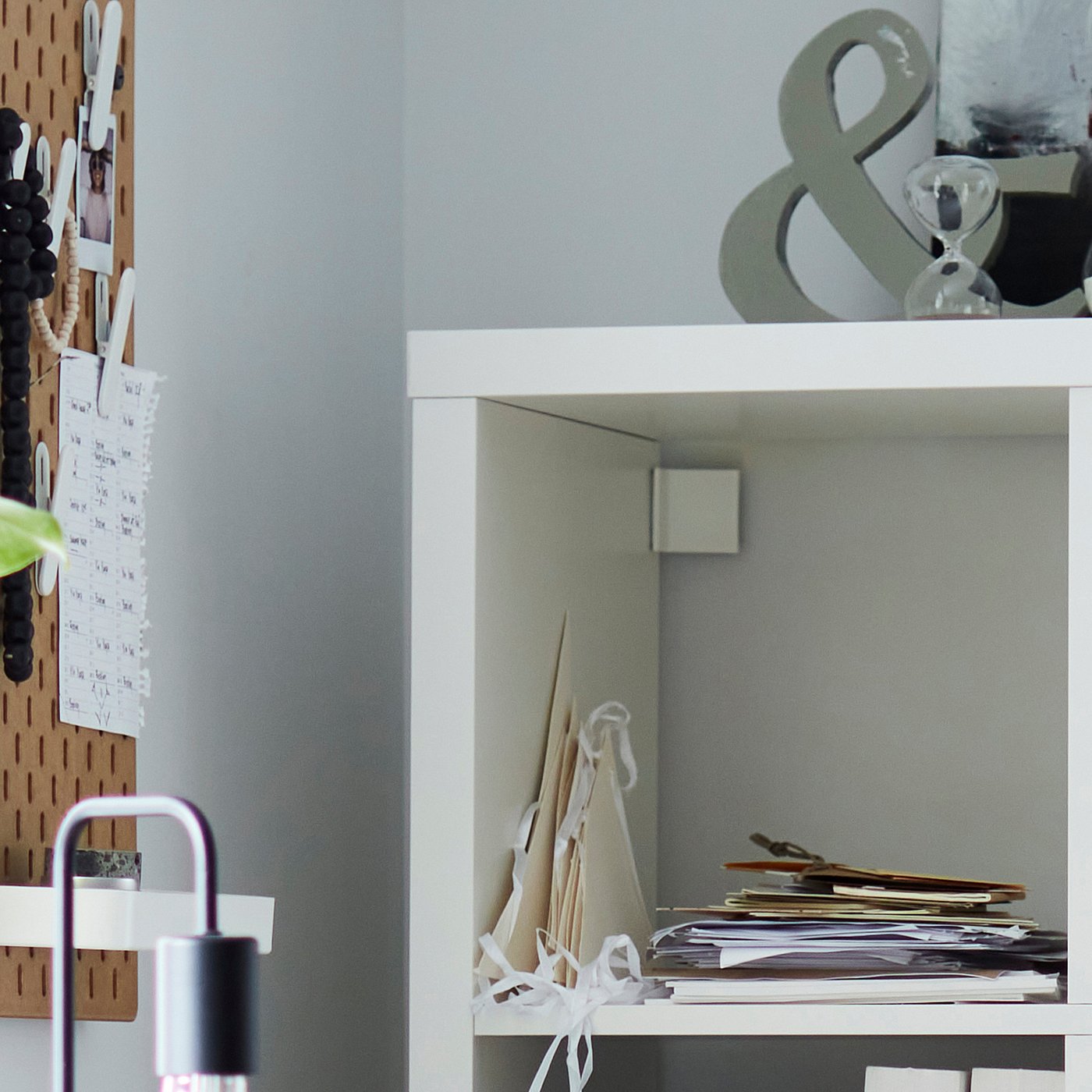 White KALLAX shelving unit with papers and a lamp on a wooden pegboard.