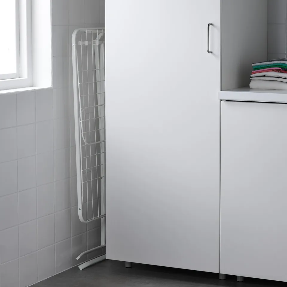 White MULIG drying rack, slim with fold-out wings for laundry, fits neatly in corner near window and cabinet.