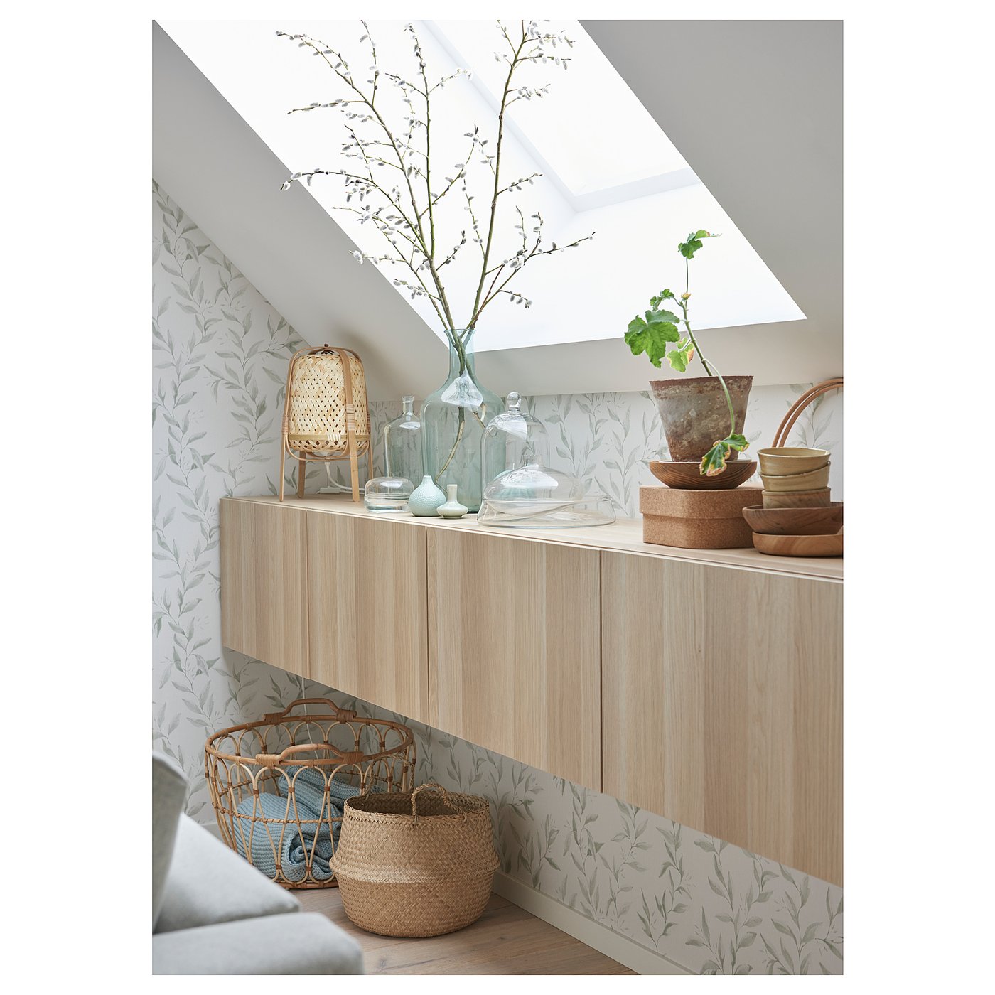 Modern living room with light wood tv unit, green plants, wicker baskets, and stylish decor against leaf-patterned wallpaper.