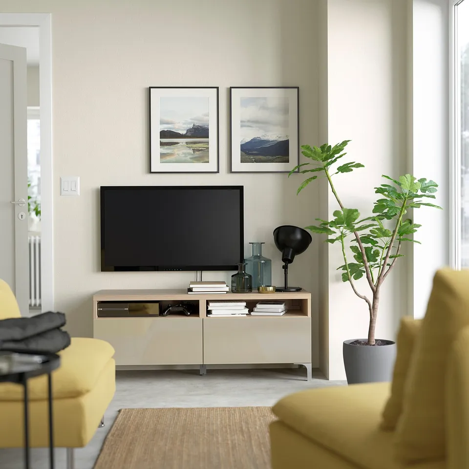 Modern living room with BESTÅ tv stand in beige, mounted flat-screen tv, yellow armchairs, and a potted plant.