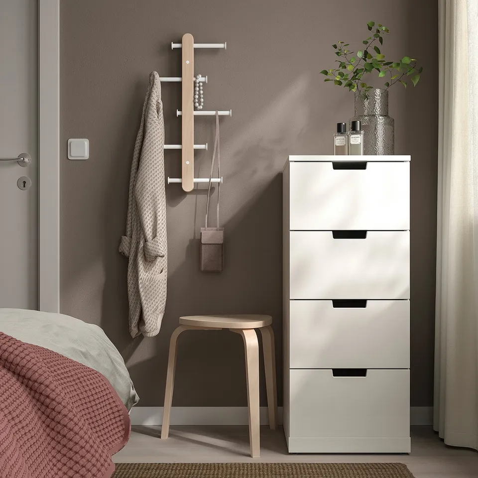 Bedroom corner with PLOGA rack, stool, and cabinet. Decorated with plants and perfume. Partial bed view.