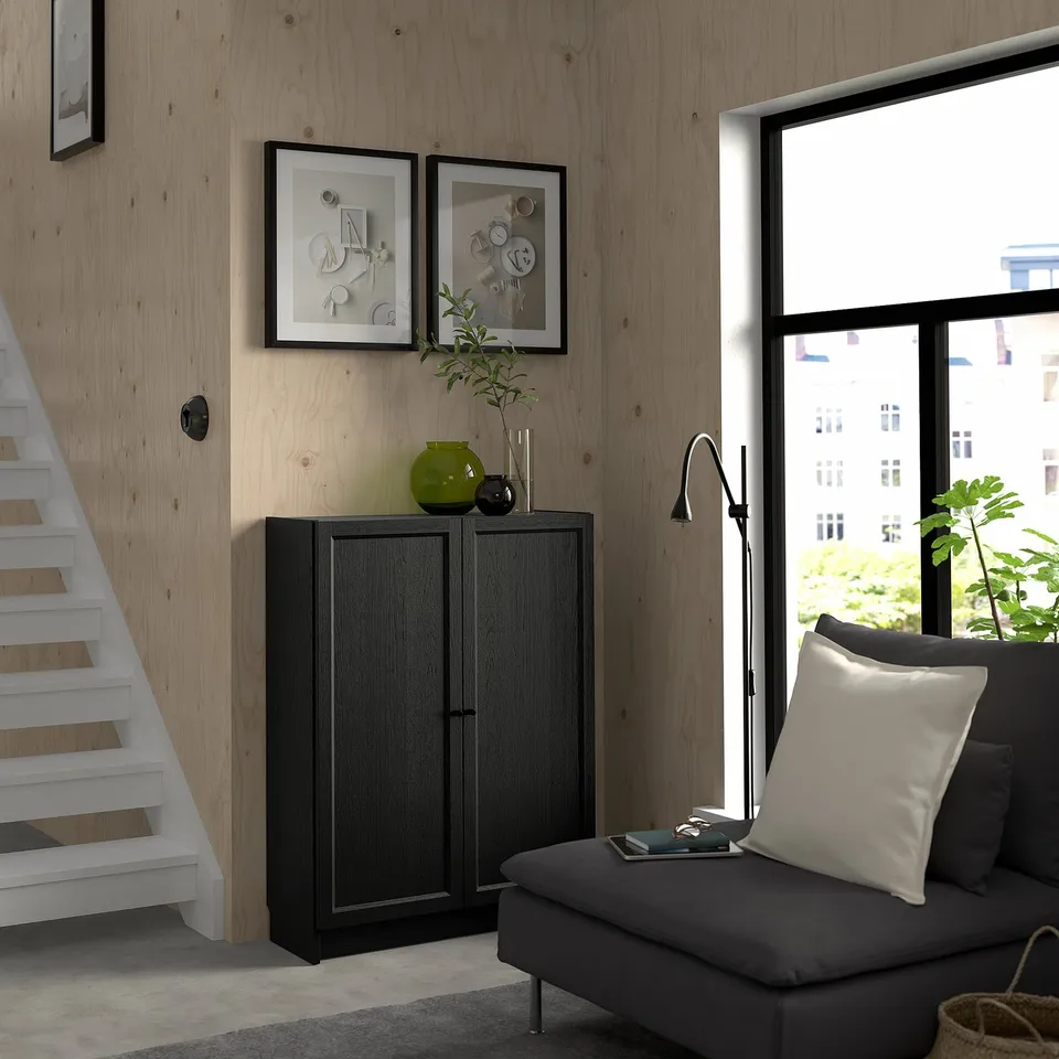 Modern living room with BILLY bookcase, plants, and grey sofa with large pillow. Large window.