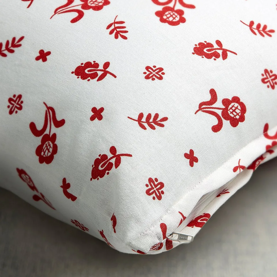 Decorative white cushion cover with red floral prints, featuring a hidden zip for easy washing.