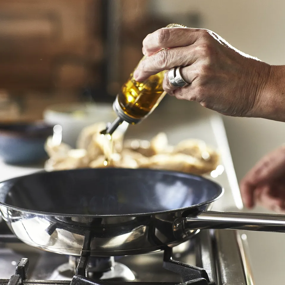 Pouring oil into non-stick skillet on stove