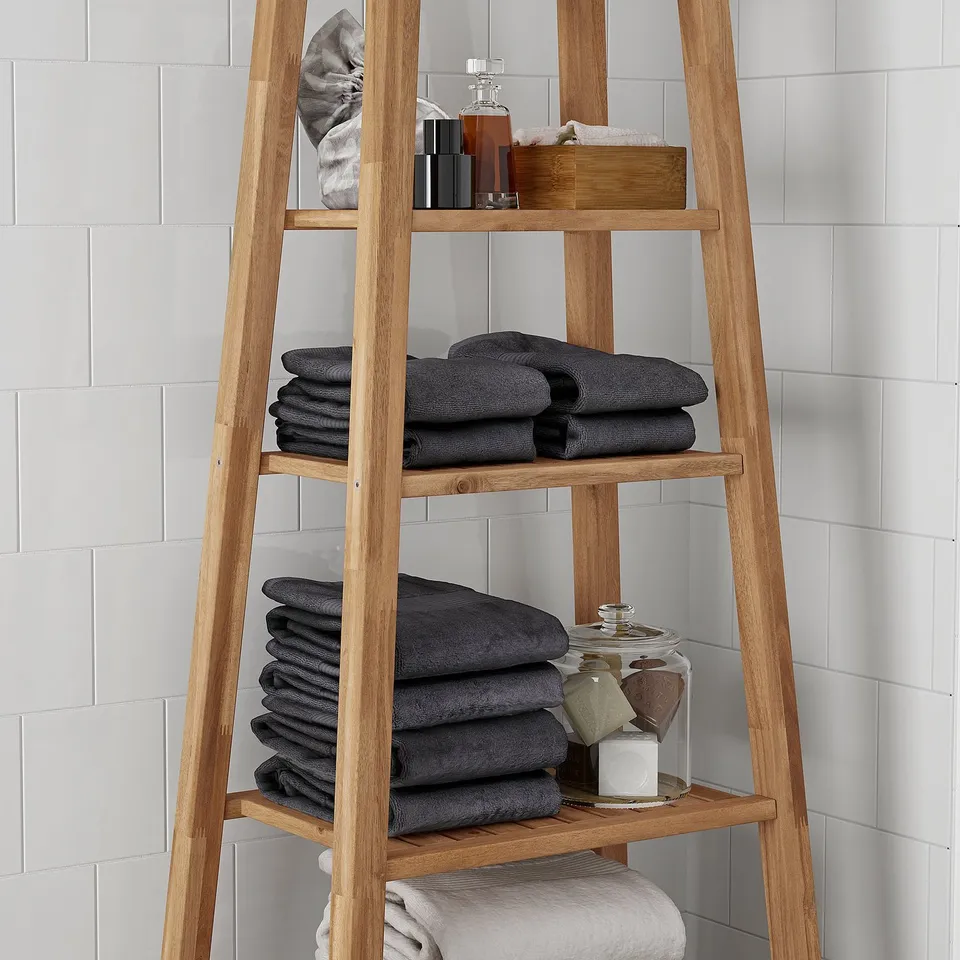 Wooden bathroom shelf holds folded dark towels and toiletries; made of durable acacia.