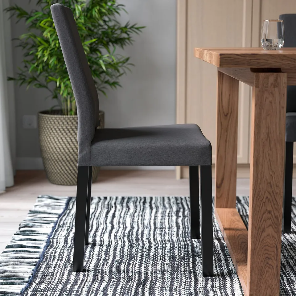 Modern chair with cushioned seat near wooden table, glass on table, patterned rug below.