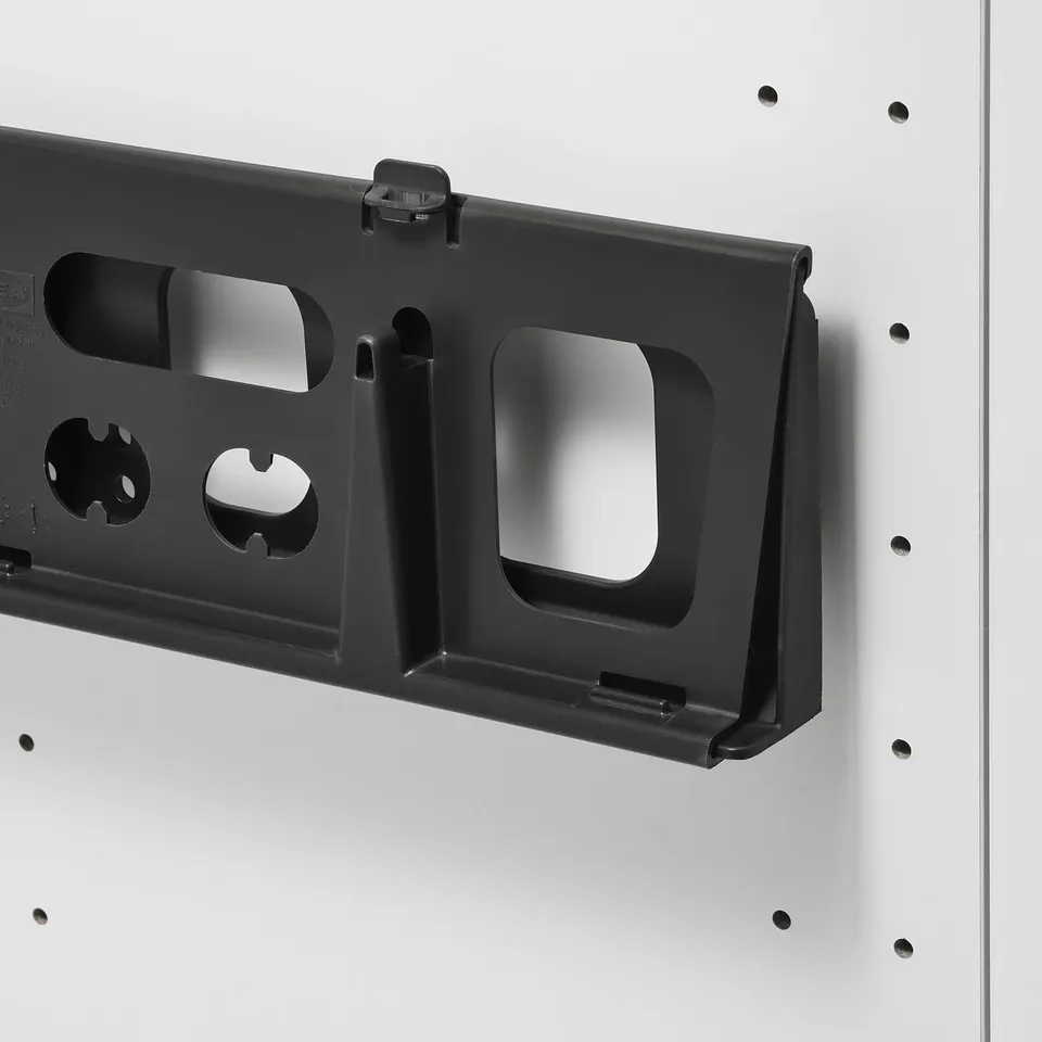 Black plastic slotted organiser attached to a white wall, designed for under-sink storage.