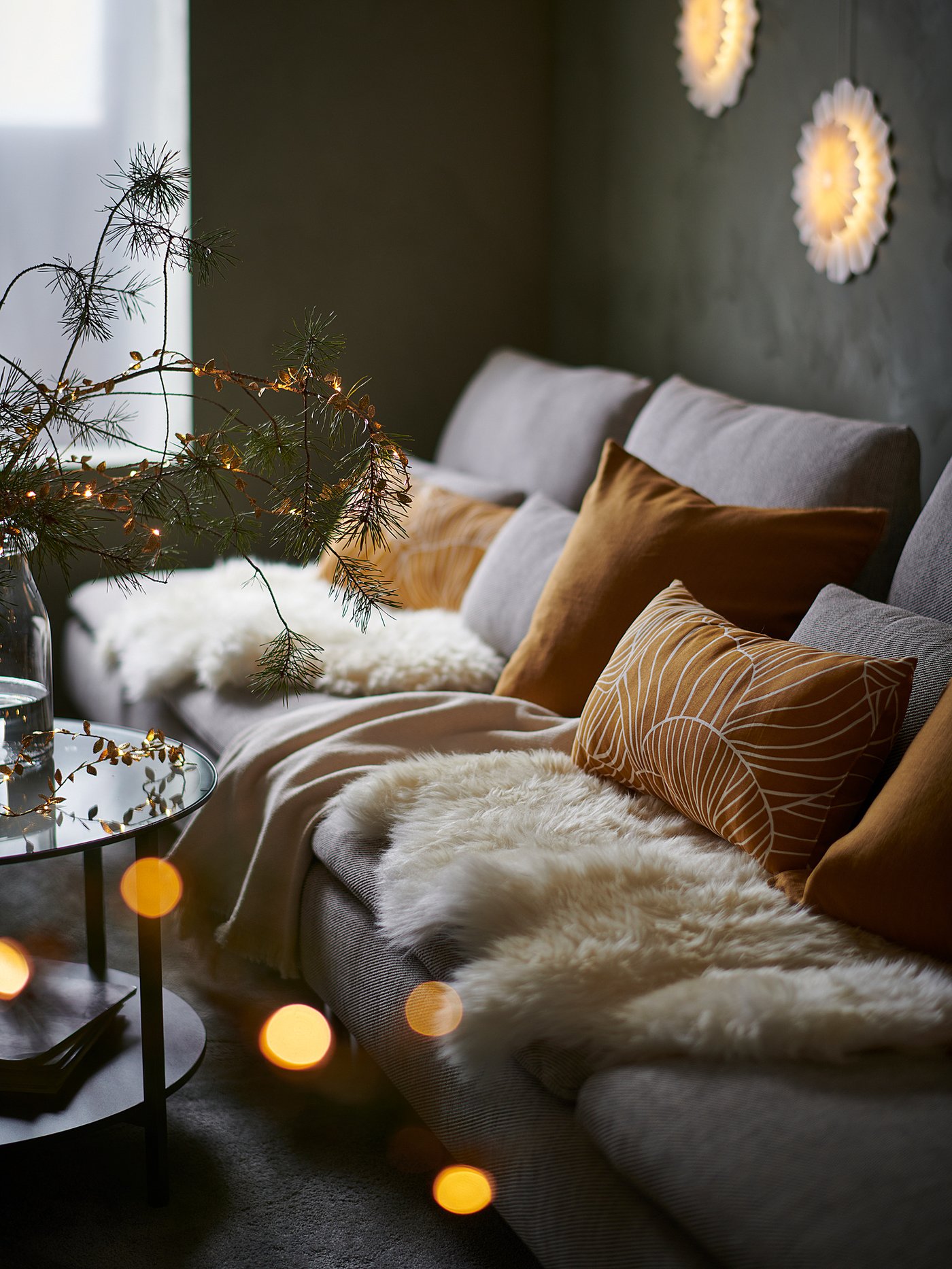 Cosy sofa with plush cushions, warm lights, and pine branches. Perfect for holiday relaxation.