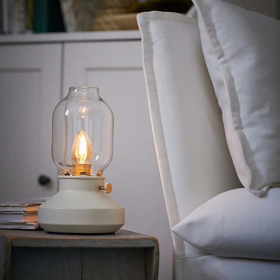 White TÄRNABY lamp with glass shade on wooden table beside chair with cushion.
