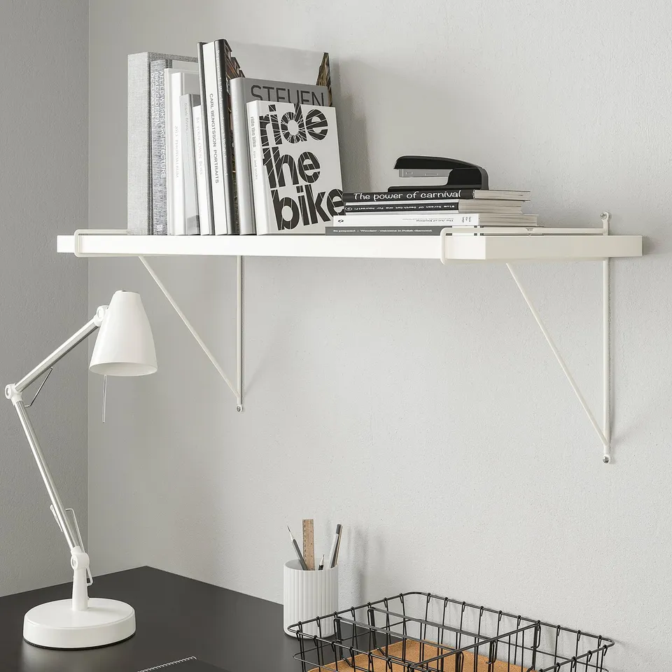 White PERSHULT wall shelf holds books, with desk lamp and pencil holder beneath.