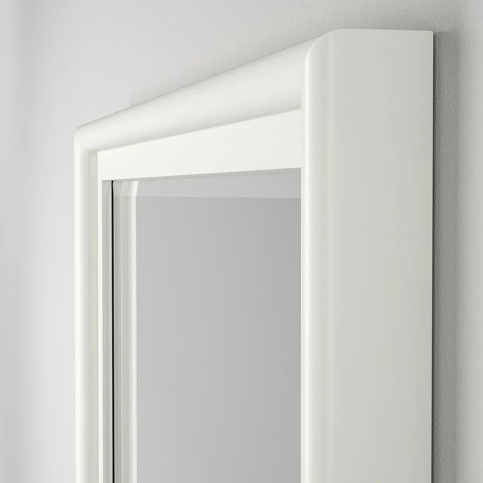 Close-up of a high-quality, white-framed mirror. The bevelled glass reflects light gently, showing craftsmanship and elegance.