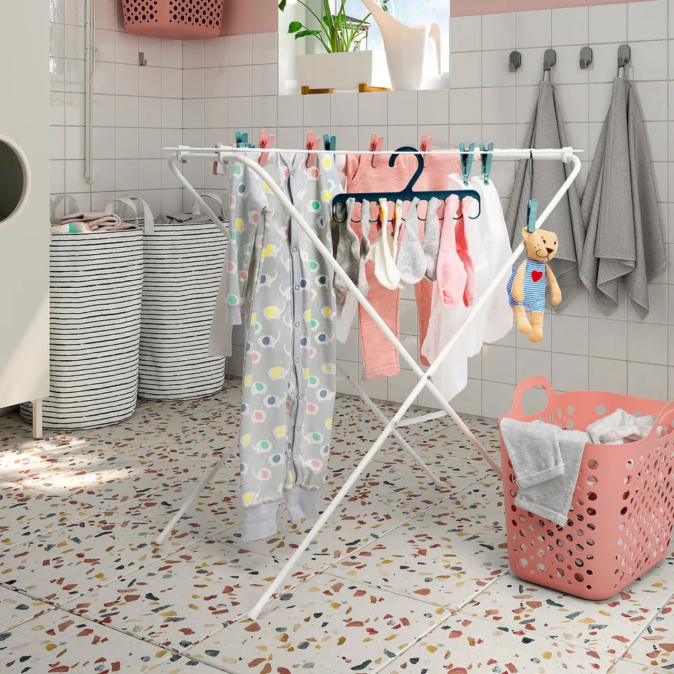 Laundry room with drying rack, colourful clothes, towels, and baskets on patterned floor.