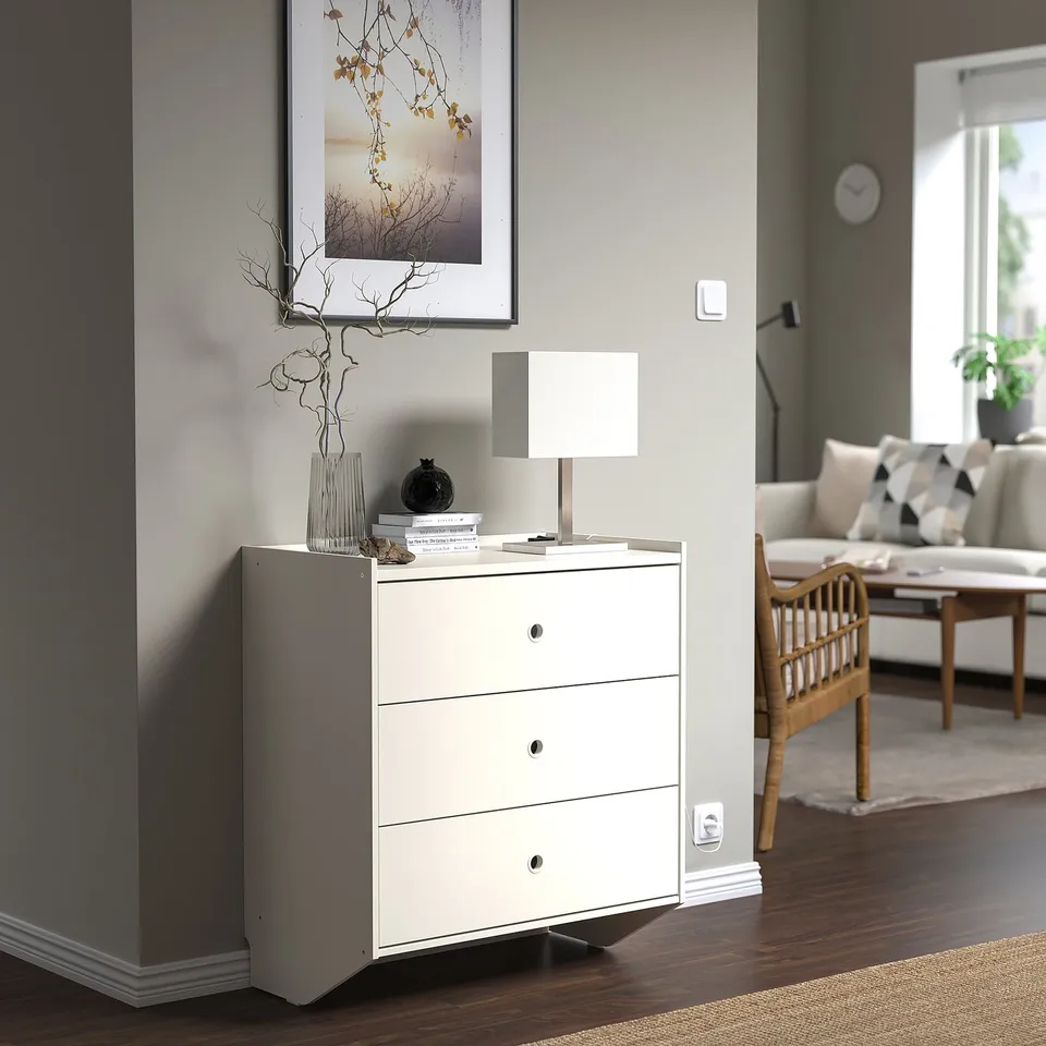 White RACKNÄS chest with 3 drawers, vase, and lamp in living space.