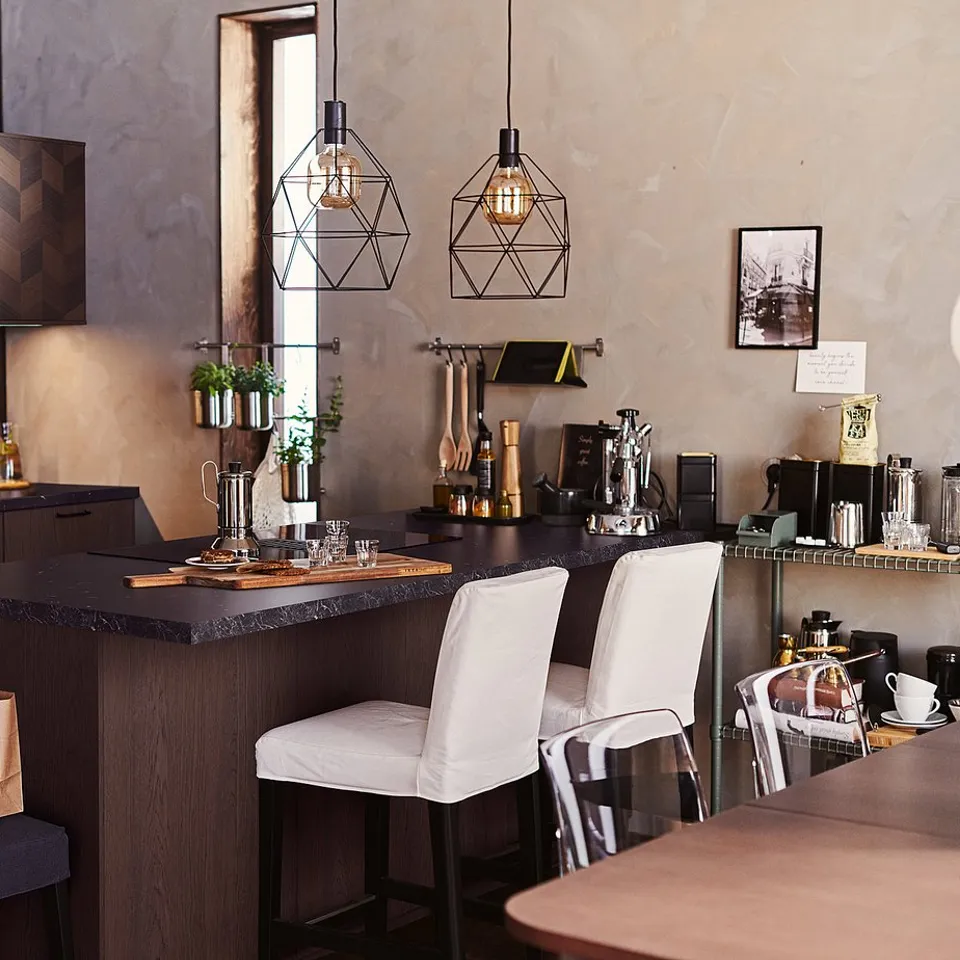 Modern kitchen with dark wood cabinets, black countertop, white chairs, hanging lights, and various kitchen appliances and utensils.