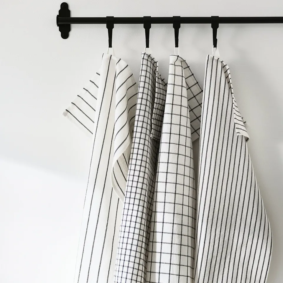 Four kitchen towels hang from a black rod, each with different striped and chequered patterns, ready for use in cleaning.