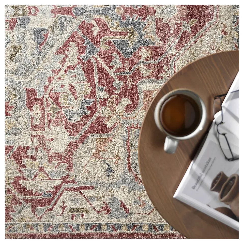 A pastel-colored, ornate rug on the floor with a wooden table displaying a mug and magazine, showcasing a stylish interior design.
