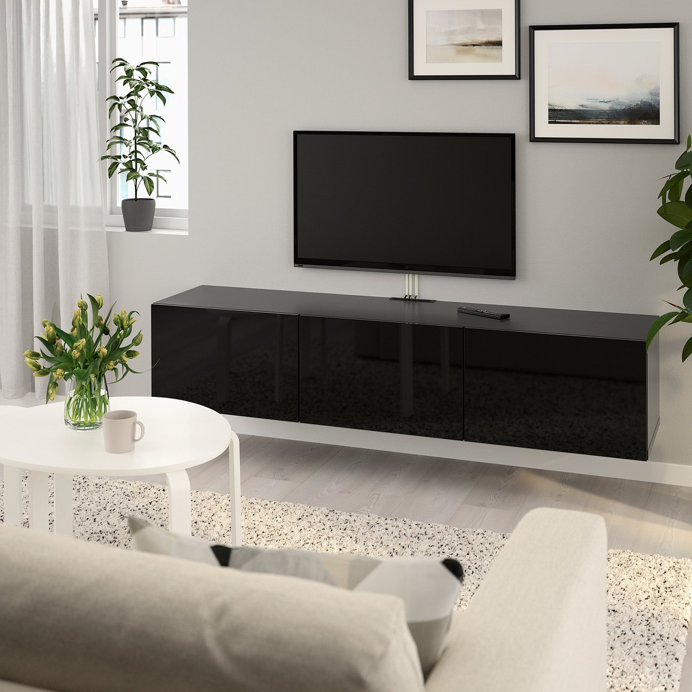 Modern living room with BESTÅ black tv bench, flat-screen tv, white side table, light sofa, plant, art.